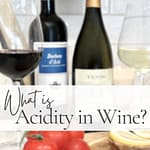 Pin graphic titled "What is Acidity in Wine?" featuring red and white wine glasses, wine bottles, tomatoes, and lemon slices on a wooden board.