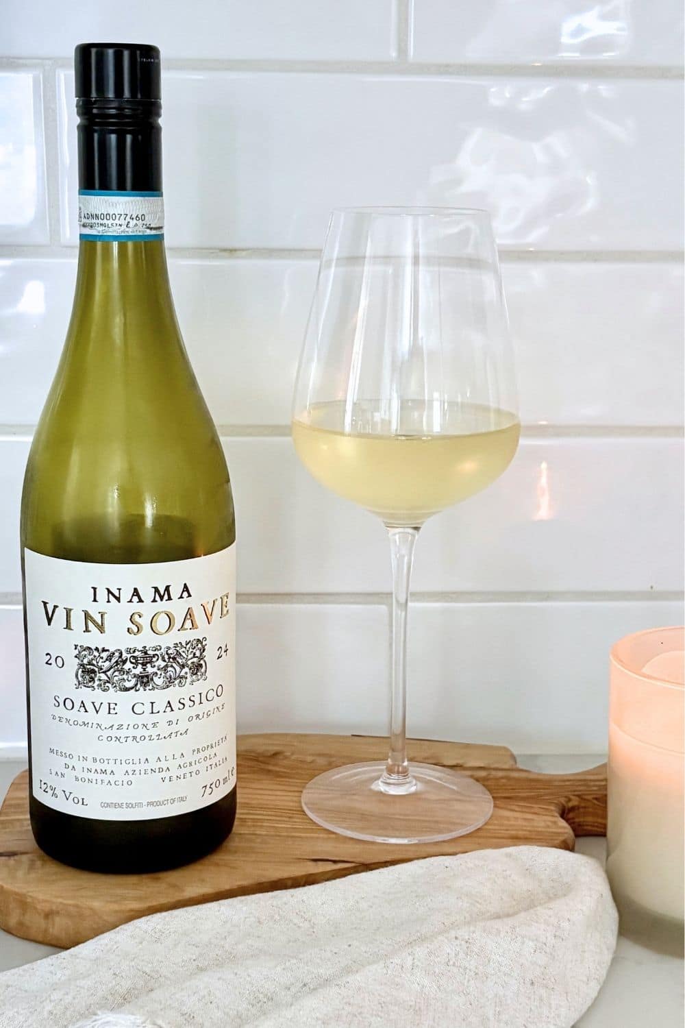 Bottle of Soave Classico Italian white wine with a glass of white wine on a wooden board in a bright kitchen setting.