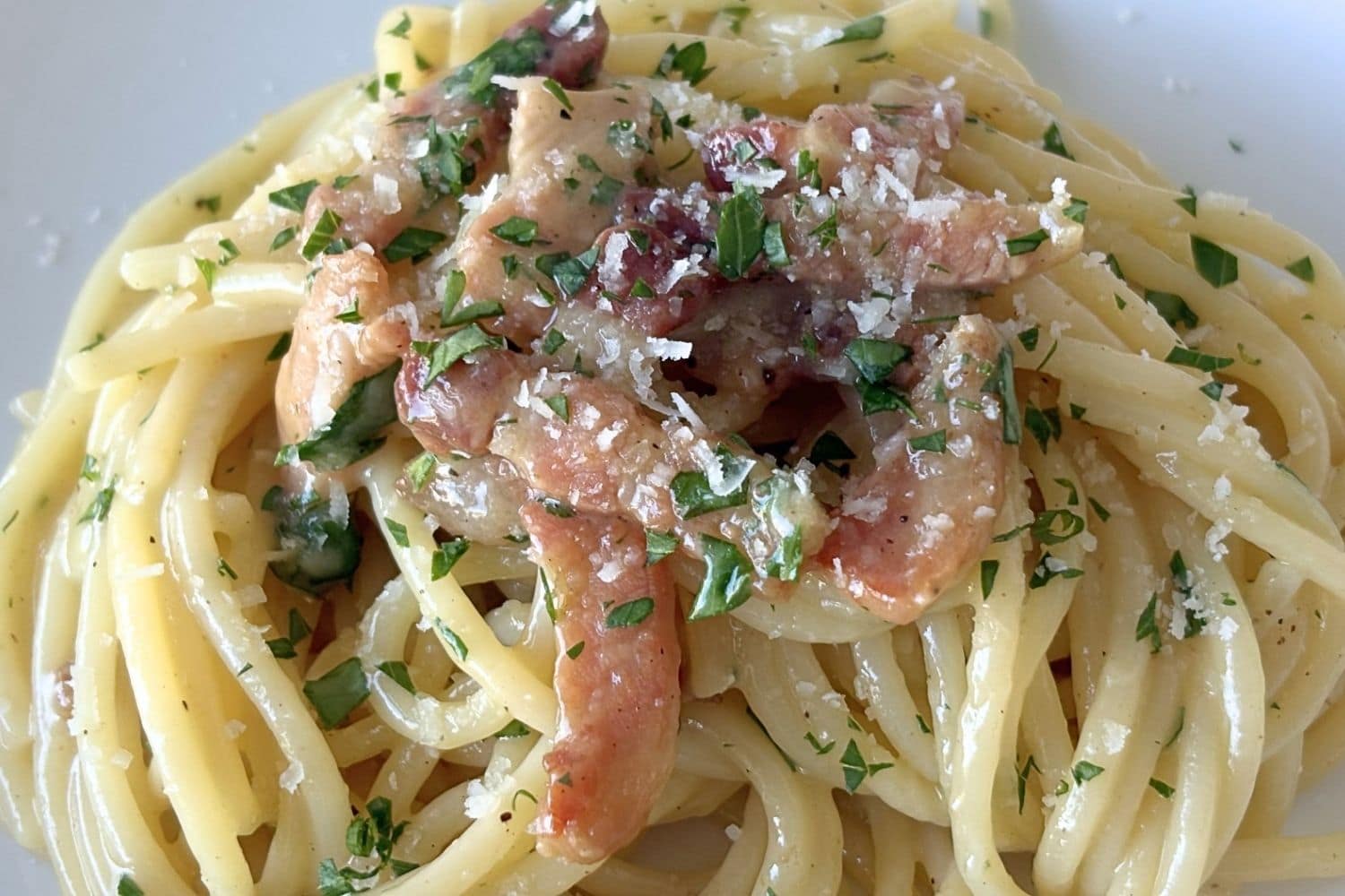 Close-up of Marcella Hazan’s carbonara sauce with spaghetti coated in a glossy egg and cheese sauce, topped with crisp pancetta, parsley, black pepper, and grated cheese.