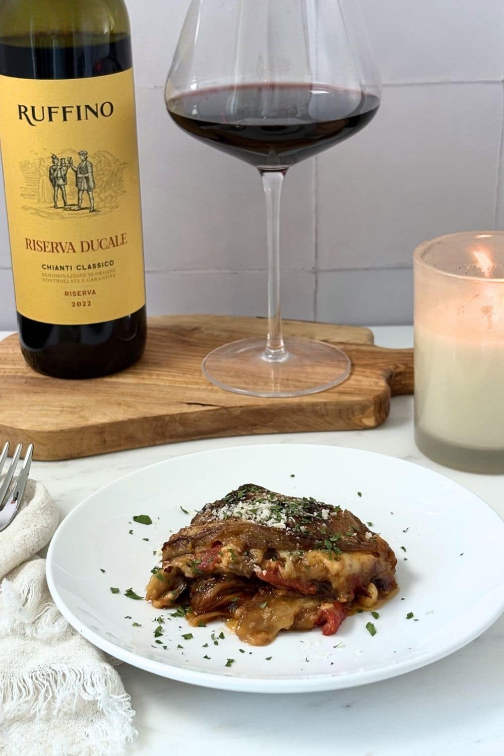 Eggplant Parmesan served with Chianti wine on a marble countertop with candlelight.