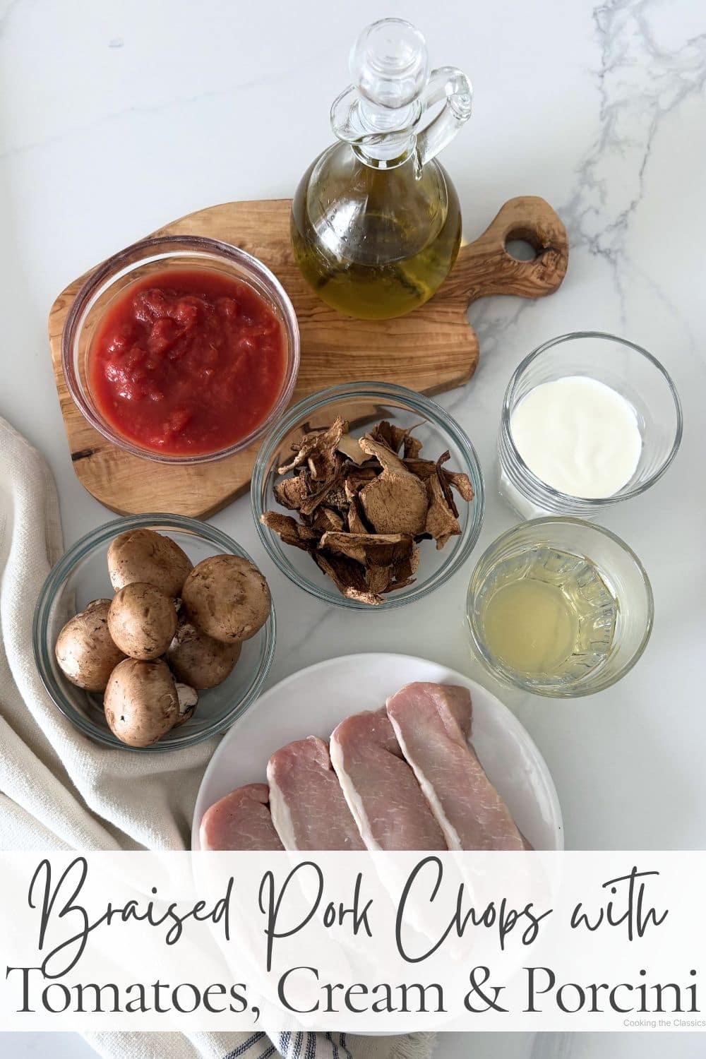Ingredients for braised pork chops with tomatoes, cream, and porcini mushrooms arranged on a marble surface