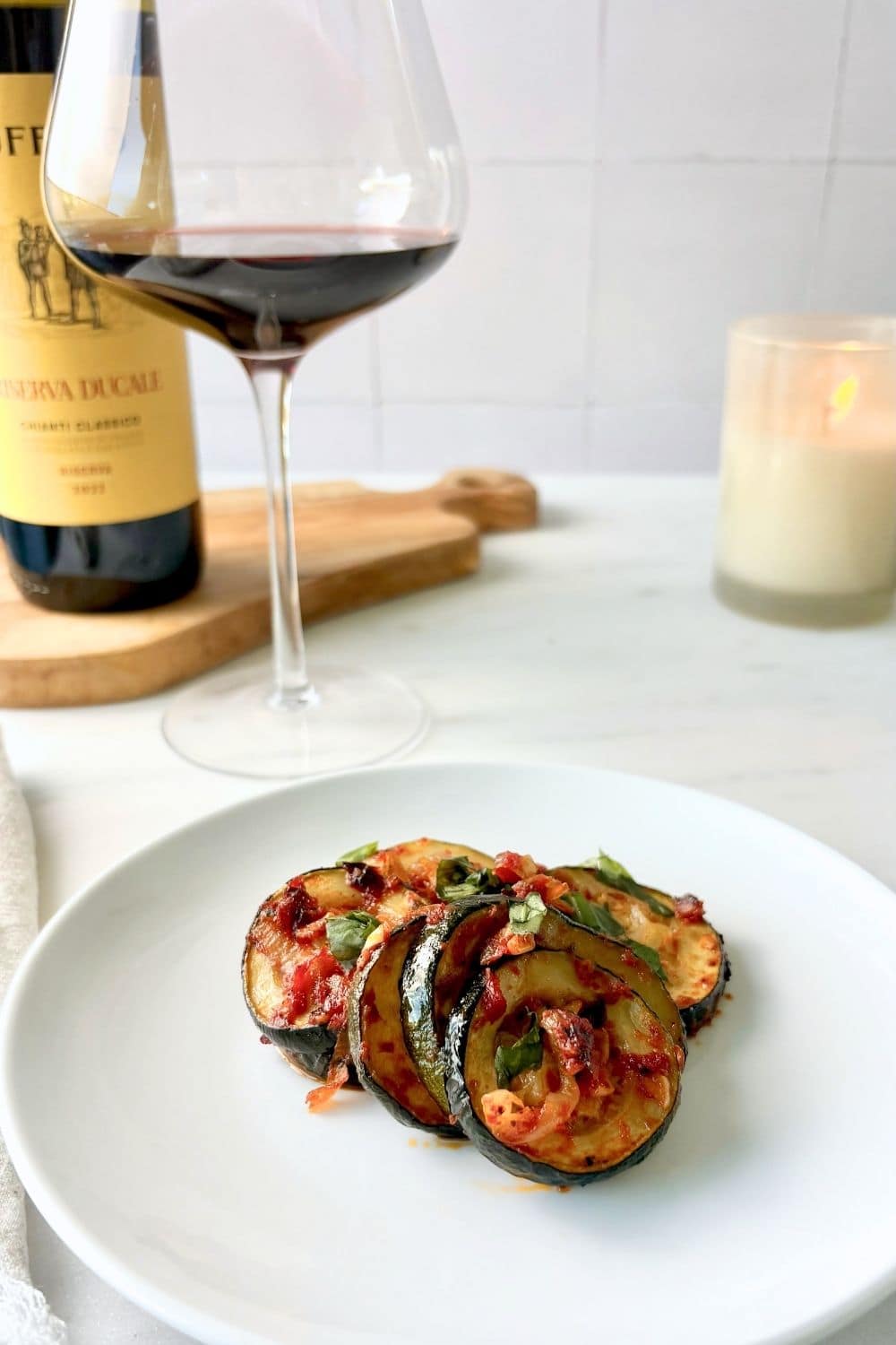 Zucchini with tomato and basil plated with a glass of Chianti and candle in the background