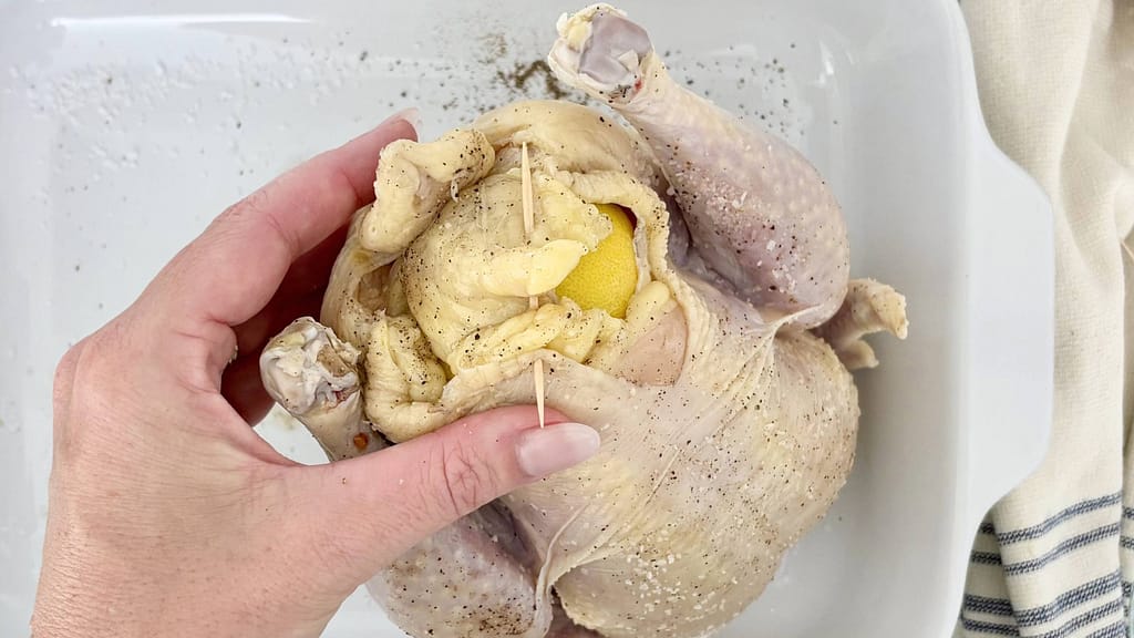 Preparing roast chicken with lemons by salting the chicken and placing lemons inside the cavity before roasting.