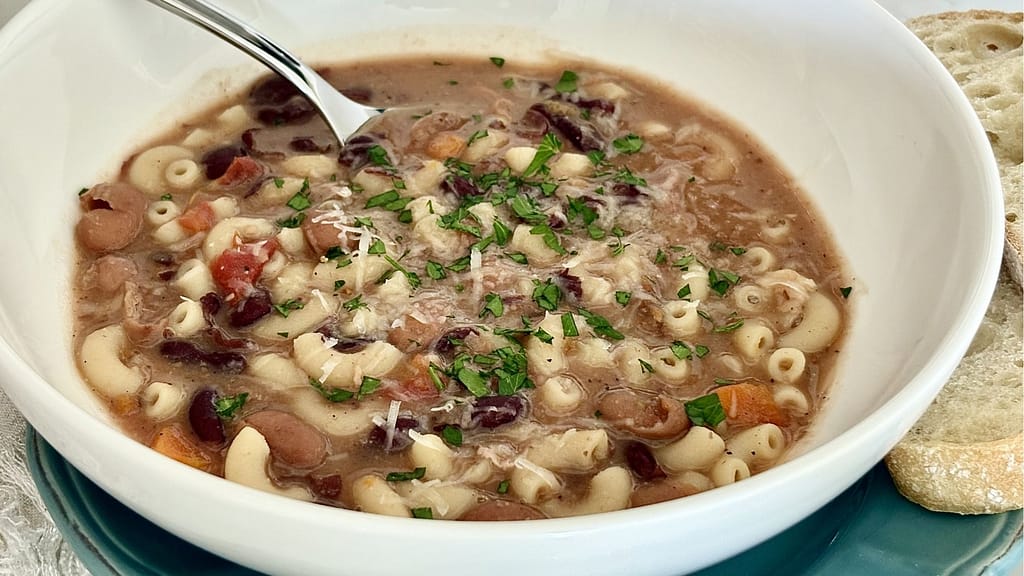 Pasta e fagioli soup with beans, small pasta, parsley, and grated cheese in a white bowl