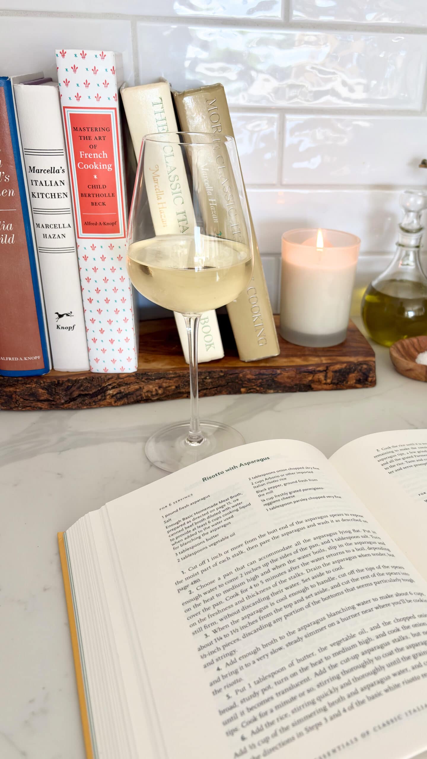 classic cookbooks next to stove with glass of wine and a book open to a recipe