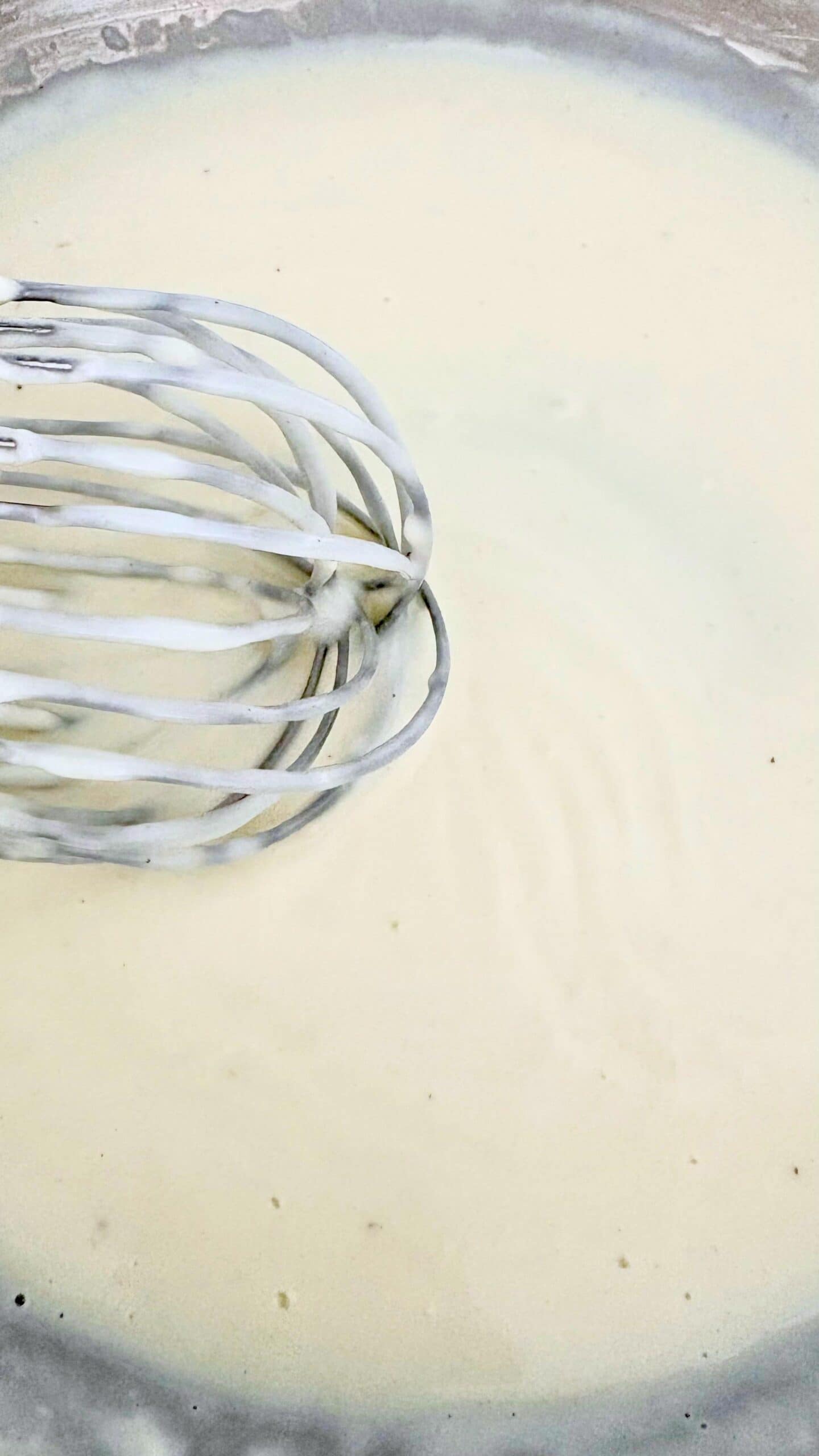 Whisk stirring a smooth béchamel sauce in a saucepan, showing the creamy texture of the classic white sauce