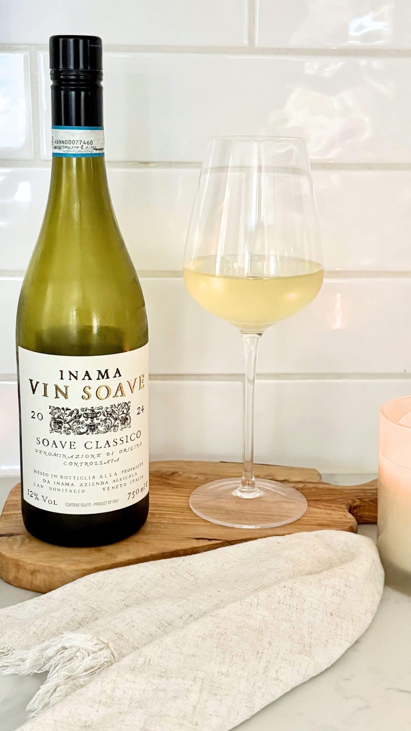 Bottle of Soave Classico Italian white wine with a glass of white wine on a wooden board in a bright kitchen setting.