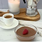 Glass bowl of Italian chocolate mousse garnished with a fresh raspberry served with a cup of espresso, a lit candle, and a stovetop moka pot.