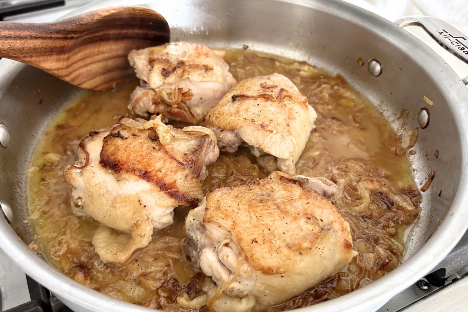 Chicken thighs browning in olive oil with thinly sliced onions, deglazed with white wine in a sauté pan