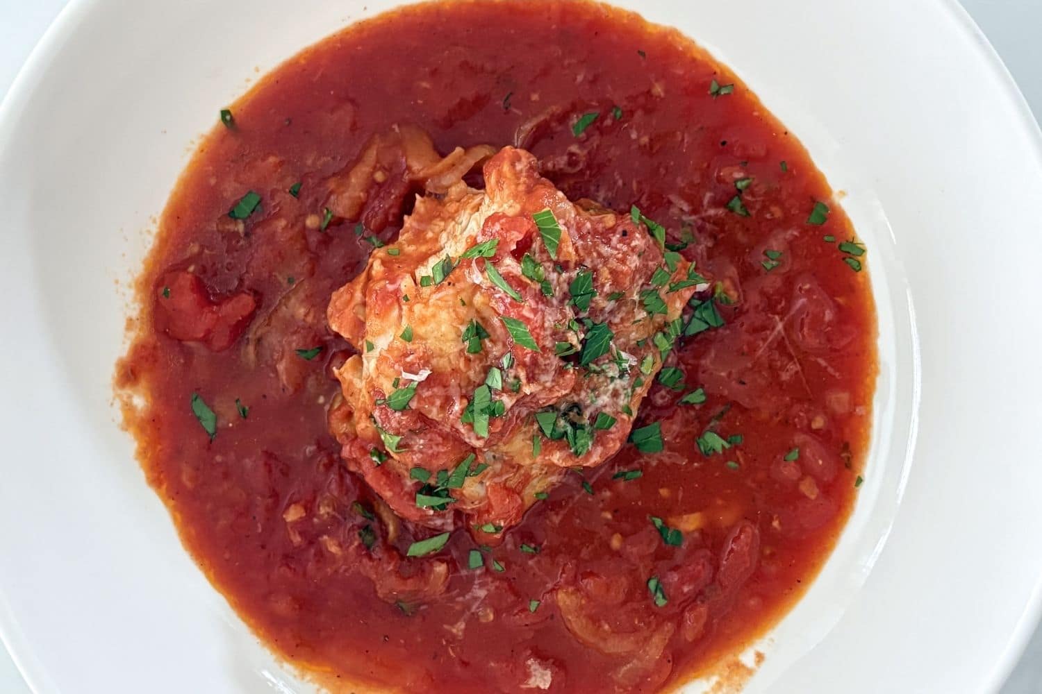 Chicken cacciatore in tomato sauce topped with parsley, served in a white bowl with tender chicken and sliced onions