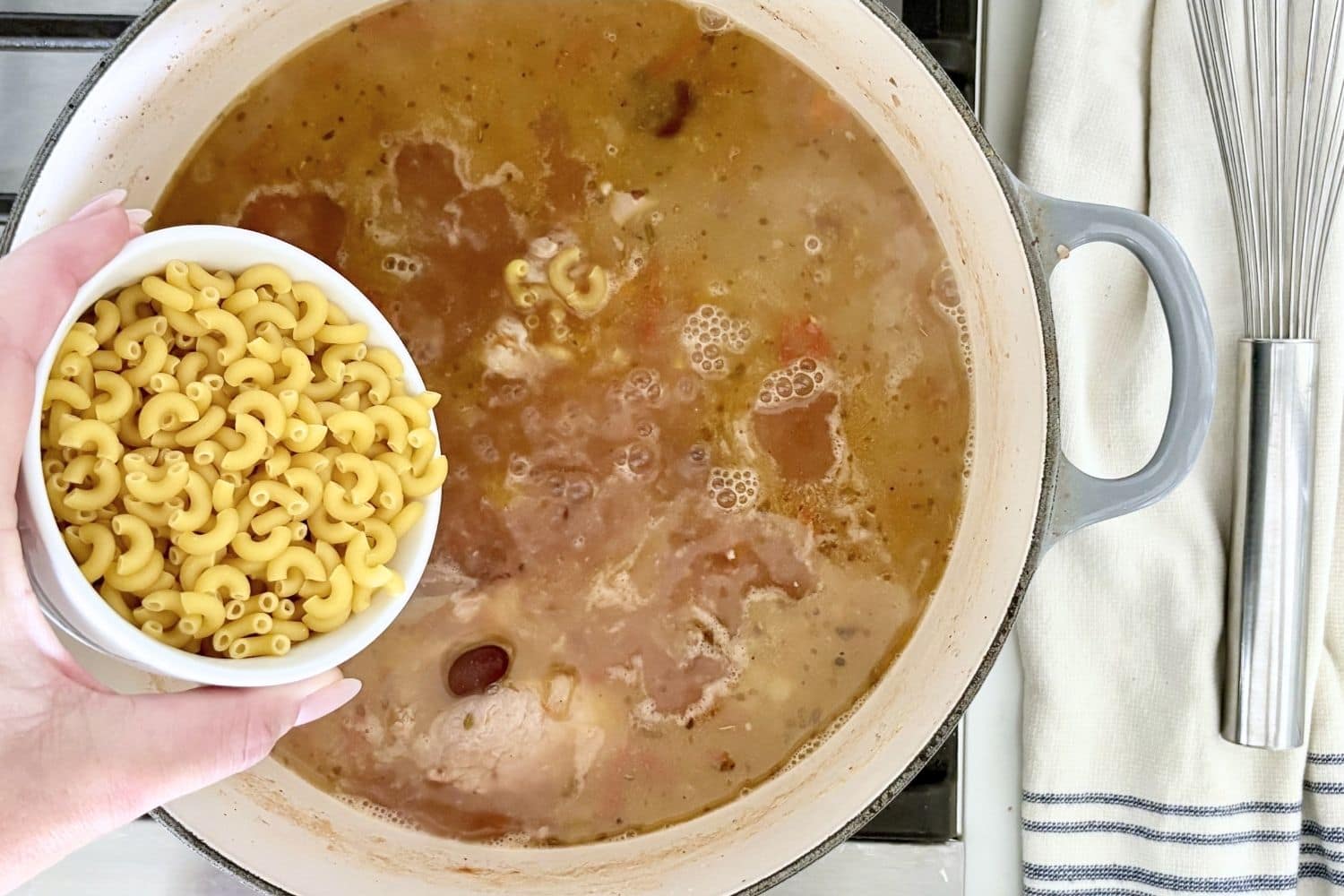 Adding small pasta to pasta e fagioli soup simmering in a pot on the stove