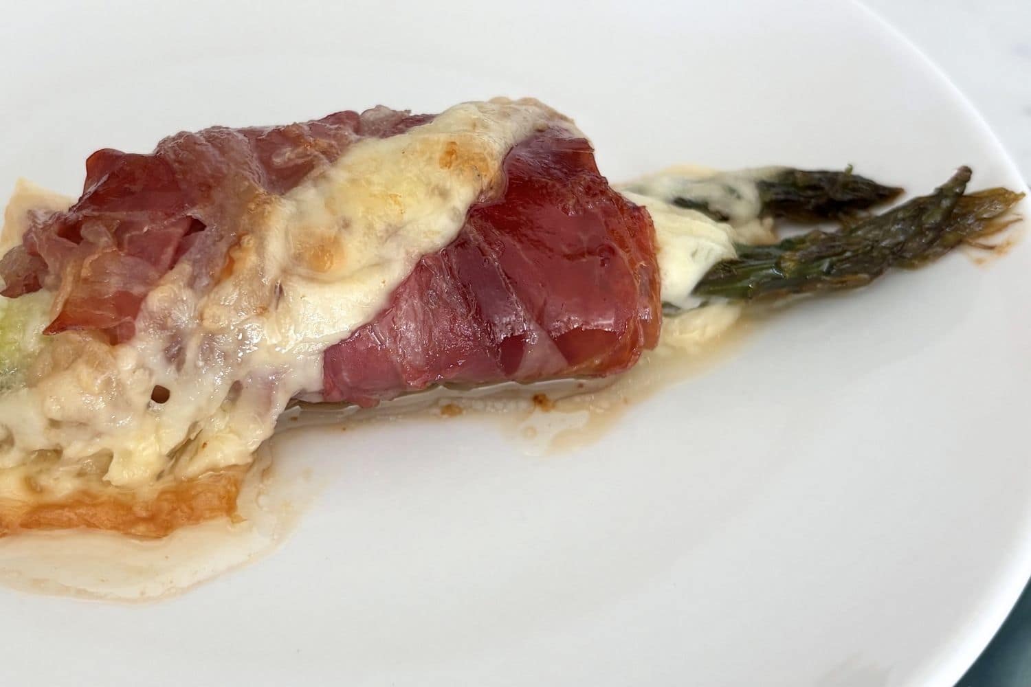 Close-up of asparagus wrapped in prosciutto and topped with melted cheese, baked until lightly golden