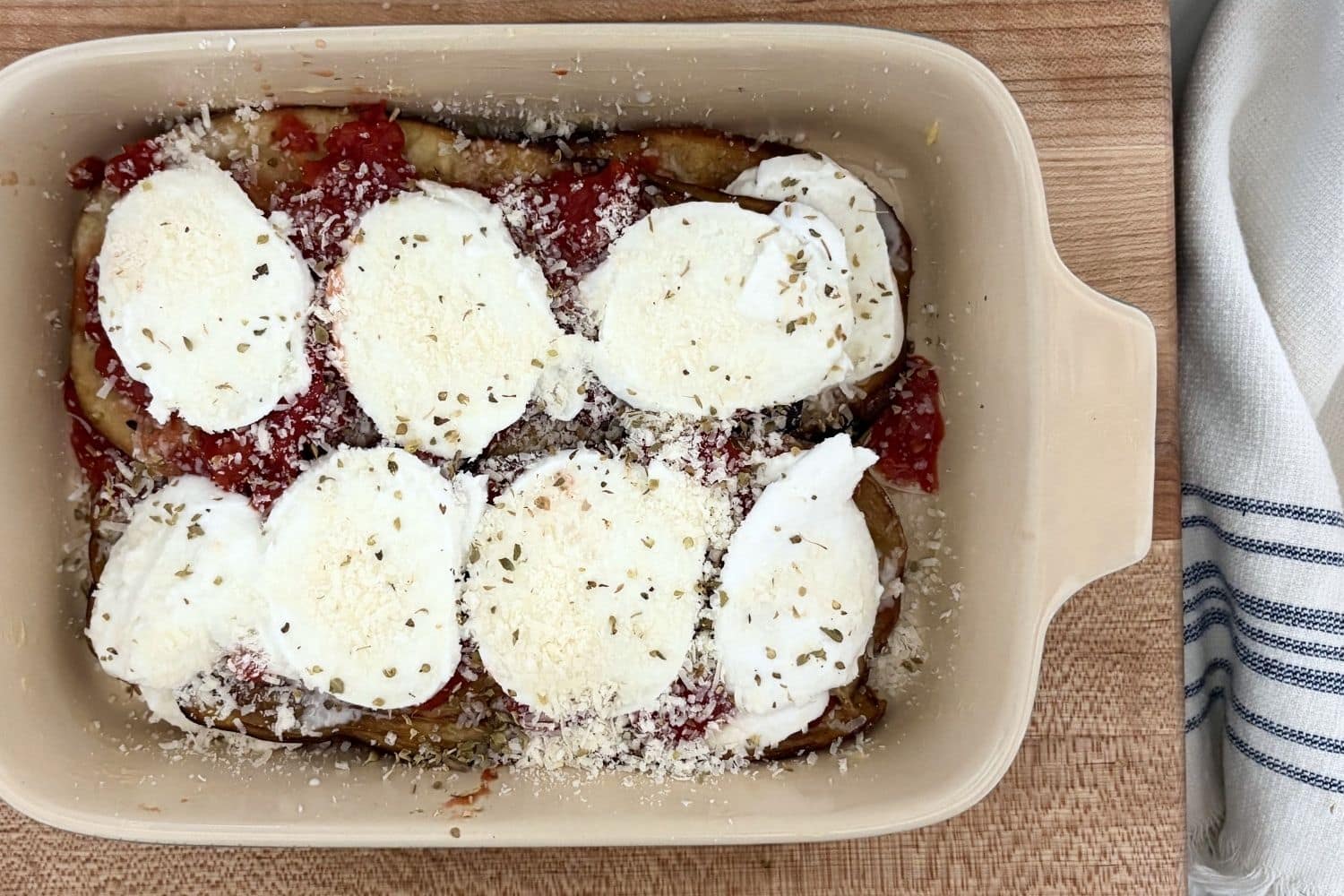 Layered Eggplant Parmesan before baking with fried eggplant, tomatoes, buffalo mozzarella, parmesan, and oregano.