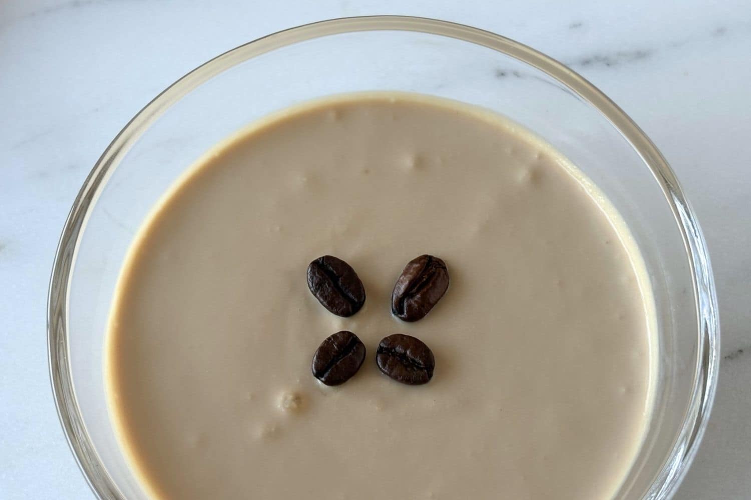 Close-up of ricotta and coffee cream dessert garnished with coffee beans in a shallow glass bowl.
