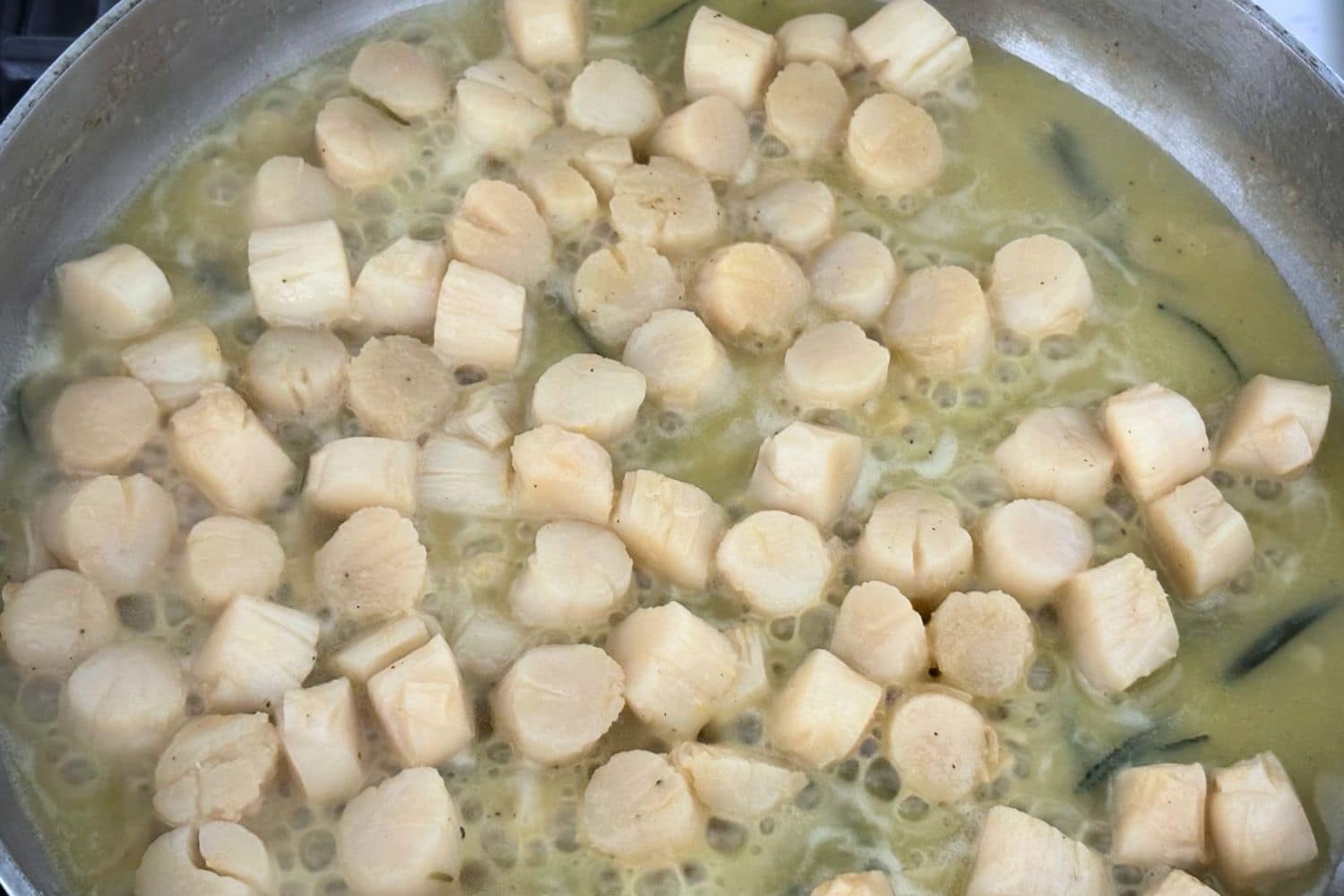 Scallops cooking in a skillet with olive oil, garlic, rosemary, and lemon sauce.