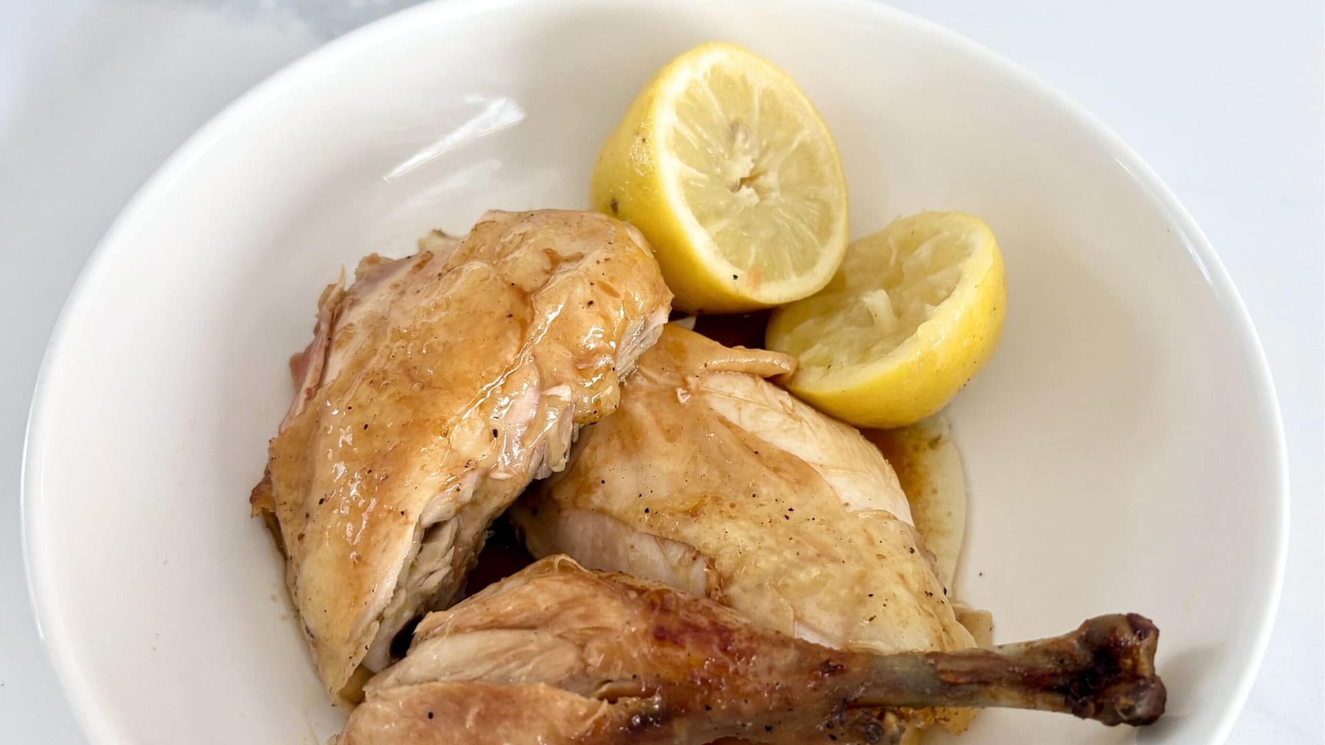 Close up of roast chicken with lemons showing crispy golden skin and juicy meat.