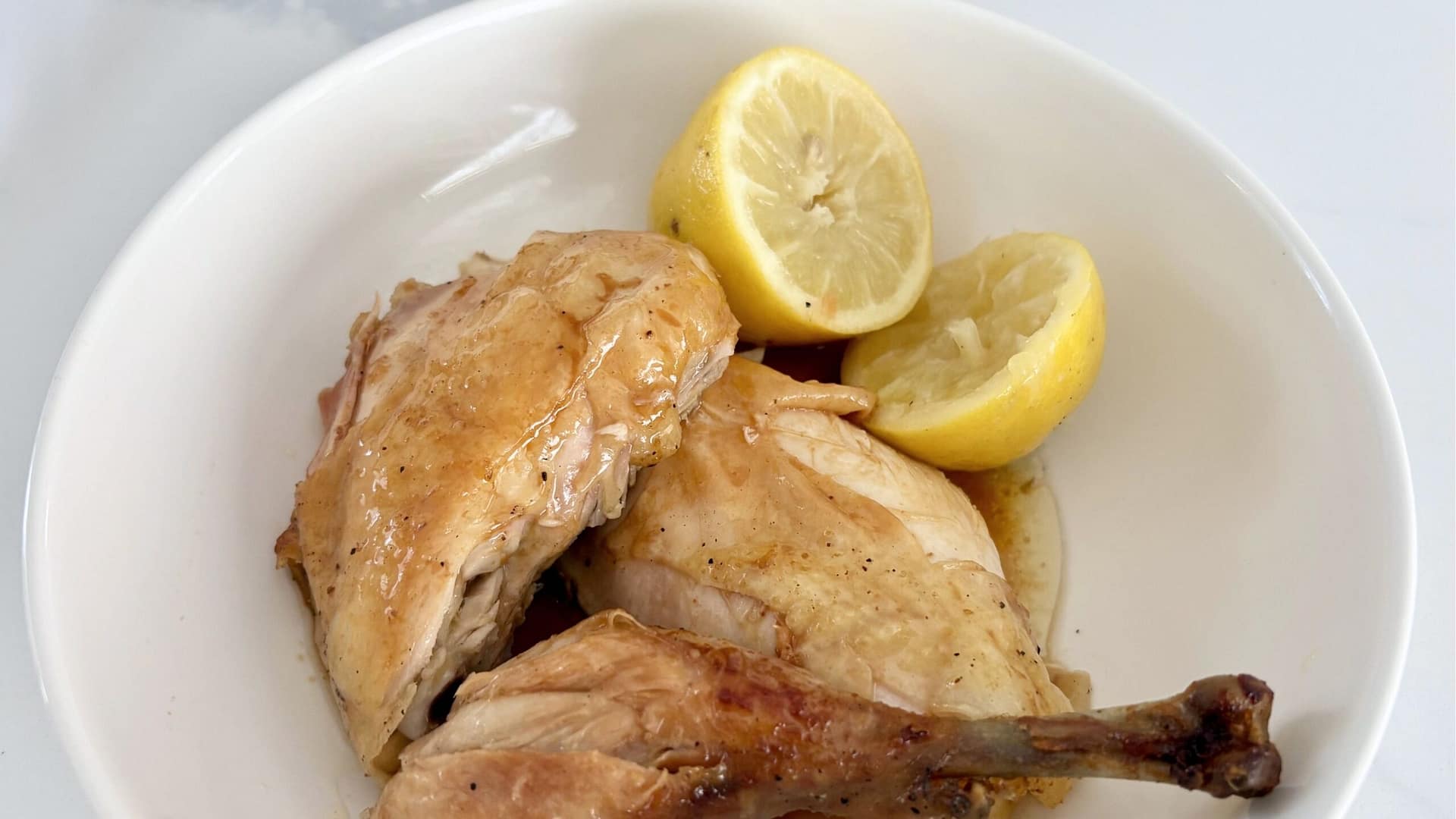 Close up of roast chicken with lemons showing crispy golden skin and juicy meat.