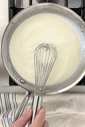 Finished béchamel sauce in a saucepan after cooking butter, flour, and milk.