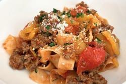 Close-up of sausage and bell pepper pasta with tomatoes and grated cheese