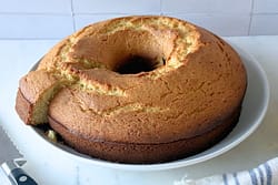 Whole olive oil cake on white platter with one slice removed showing tender crumb.