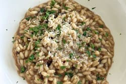 Creamy risotto with porcini mushrooms topped with grated Parmesan and chopped parsley in a white bowl.