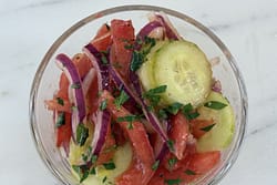 Glass bowl filled with tomato, cucumber, onion, and basil salad made with peeled tomatoes, thin cucumber slices, red onion, and fresh basil.