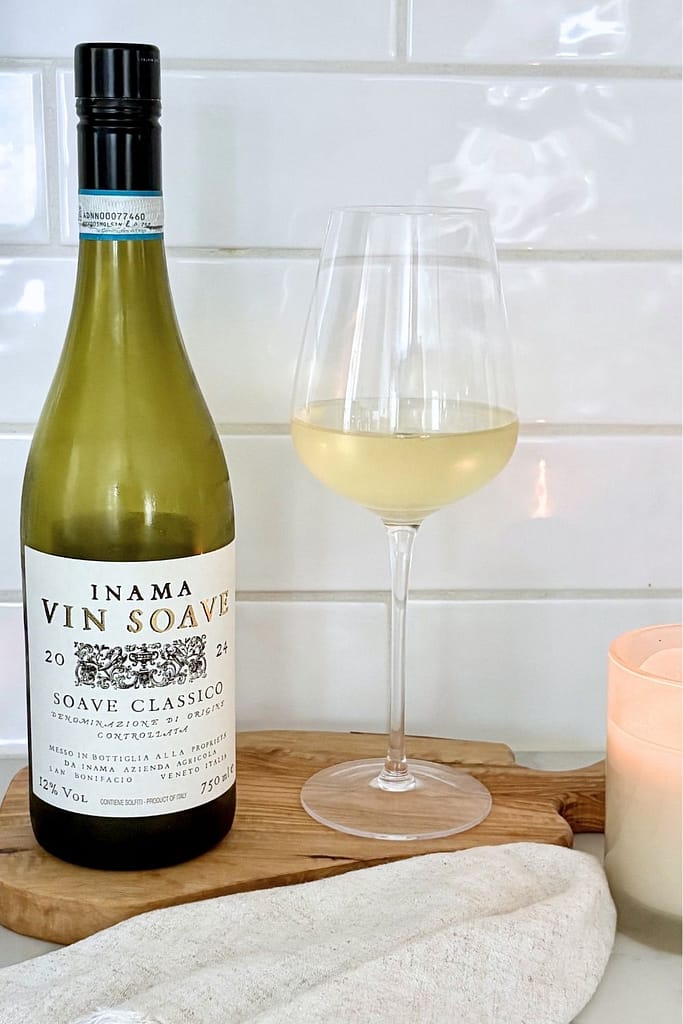Bottle of Soave Classico Italian white wine with a glass of white wine on a wooden board in a bright kitchen setting.